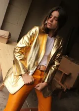 Blazer de cuero color fucsia con aberturas laterales y aplique tipo pin desplegable bañado en bronce, complementado con botones de nácar.