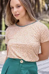 Remera color beige con estampado de pequeñas flores blancas y cuello redondo con borde verde.