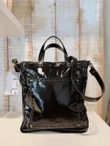 Bolso tote de cuero charol negro con doble asa corta y correa larga extraíble.