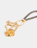 Llavero con correa de strass gris y dijes dorados: rosa, corazón y moño.