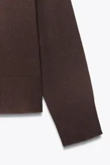 Jersey de punto color verde oliva, con cuello redondo y manga larga. Tiene bajo con aberturas laterales y acabados en rib.