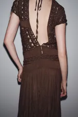 Vestido largo color marrón con detalle de crochet en el corpiño, escote redondo y manga corta. Cierre en la espalda con lazadas.