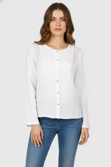 Camisa blanca de algodón con cuello a la base, cierre frontal con botones y apliques de encaje en los hombros.