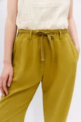 Pantalón babucha de tiro alto confeccionado en símil lino color verde oliva. Tiene calce relajado que ajusta hacia el ruedo y largo hasta los tobillos, cintura elastizada con lazo de ajuste, bolsillos diagonales en laterales y dos bolsillos ojal falsos en espalda.