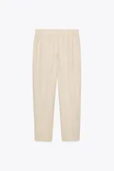 Pantalón color crema de tiro alto con pinzas delanteras y cintura elástica en la espalda. Tiene bolsillos delanteros y traseros.