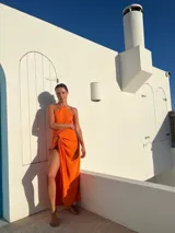 Vestido largo naranja de crepé con escote halter y falda tipo pareo con abertura lateral.