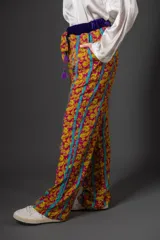 Pantalón de viscosa con estampado floral en tonos fucsia y amarillo, con rayas verticales turquesas. Presenta cintura elastizada con detalle de terciopelo violeta y lazo con borlas.