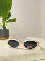 Lentes de sol color crema con forma ovalada y protección UV400.