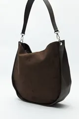 Bolso tipo hobo de cuero sintético negro con panel frontal de gamuza. Tiene correa de hombro ajustable y logo metálico plateado.