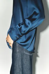 Camisa azul marino de satén con cuello solapa, escote en pico y mangas largas con puños abotonados.