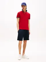 Chomba Tommy Hilfiger roja de algodón elástico, con cuello tejido a contraste en azul marino y ribetes blancos. Logo bordado en el pecho y tapeta de dos botones.