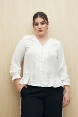 Camisa blanca de manga larga con escote en V y botones forrados al tono en el frente. Destaca por su textura sutil y por el detalle de frunces con volados en la parte inferior.