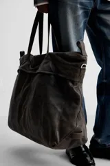 Bolso de viaje marrón oscuro fabricado en piel con acabado craquelado. Tiene un compartimento principal con cierre de cremallera, un bolsillo plano interior con cremallera y dos bolsillos frontales con botón a presión. Cuenta con asas de mano de piel y asa de hombro removible y ajustable.