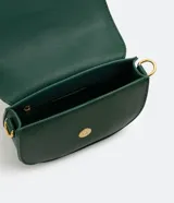 Bolso saddle pequeño color verde esmeralda, con solapa frontal con hebilla metálica dorada y cierre con botón a presión. Incluye correa transversal de grosgrain extraíble y bolsillo interno con cremallera.