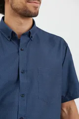 Camisa de manga corta azul con estampado de lunares blancos, cuello button-down y bolsillo en el pecho.