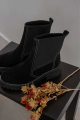 Bota corta negra de gamuza y neopreno, con elástico lateral y costuras blancas. Tiene suela track y tirador trasero.