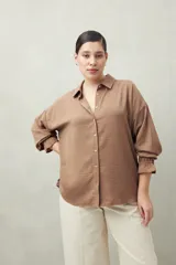 Camisa negra de manga larga con cuello clásico y botones frontales. El tejido presenta una textura arrugada o plisada, y los puños tienen un detalle fruncido o elástico.