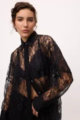 Camisa negra de encaje con cuello clásico, cierre frontal con botones y mangas largas con puños abotonados.