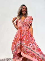 Vestido largo de corte evasé con estampado floral en tonos rosados y anaranjados. Tiene escote en V cruzado, mangas cortas con volantes y falda con volantes asimétricos.