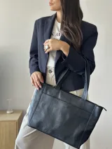 Cartera tipo tote de cuero graneado color negro, con textura uniforme y suave al tacto. Tiene manijas de 55 cm, bolsillo frontal con broche imantado, bolsillo trasero con cierre metálico, cierre principal metálico, forro interior y tres bolsillos internos (uno con cierre, uno plaqué y uno tipo sobre con solapa y botón).