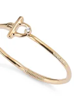Pulsera rígida dorada con cierre frontal en forma de estribo y un pequeño topacio blanco engarzado.