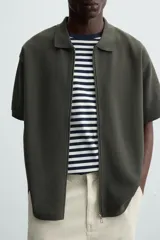 Chaqueta color beige de tejido con mezcla de algodón, corte relaxed fit, cuello solapa, manga corta y cierre frontal con cremallera.