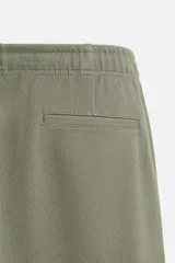 Pantalón de jogging color beige confeccionado en tejido de mezcla de algodón. Cuenta con cintura elástica ajustable con cordón, bolsillos frontales y traseros.