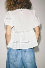Blusa negra de algodón con cuello redondo y manga corta abullonada. Presenta bordados a tono y cierre en la espalda con abertura y botón.