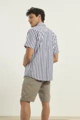 Camisa de manga corta a rayas verticales azules y blancas, con cuello abotonado y bolsillo en el pecho.