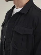 Camisa gruesa de gabardina color azul marino, con cuello clásico, cierre frontal con botones a presión, cuatro bolsillos frontales con solapa y puños abotonados.