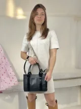 Bolso negro de cuero con detalles charolados, doble asa corta y correa larga de tela con el nombre de la marca.