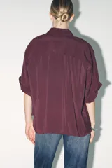 Camisa color borgoña de corte amplio, confeccionada en tejido fluido con modal. Tiene cuello solapa, manga corta con dobladillo y cierre frontal con botones.