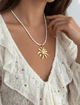Collar con tiento trenzado blanco y dije metálico dorado con forma de sol estilizado.