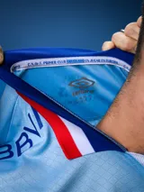 Camiseta de fútbol celeste con cuello y mangas con detalles en azul y rojo. Incluye logo de Umbro, escudo del Club Nacional de Football y sponsor Antel.