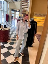 Camisa celeste y blanca a rayas verticales, con botones metálicos a presión, corte relajado y cuello clásico.