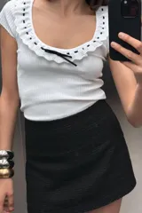 Camiseta blanca de canalé con escote redondo, manga corta y detalle de volantes con cordón negro a contraste.
