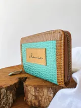 Billetera pequeña de cuero turquesa con textura de reptil y detalles en cuero marrón. Tiene cierre metálico y monedero interno.