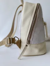 Mochila pequeña de cuero color gris claro y beige, con cierre superior y bolsillo frontal con cierre. Tiene asa de mano y correas ajustables para los hombros.