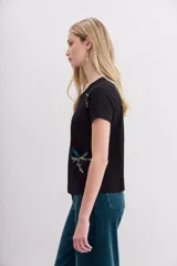 Remera de mangas cortas color crudo, de calce relajado y escote redondo. El frente se encuentra bordado con un diseño de palmeras en lentejuelas y canutillos.