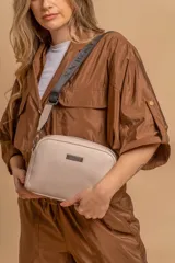 Bandolera pequeña de textura símil cuero color caramelo/marrón, con dos compartimentos principales con cierre. Correa ancha ajustable de tela negra con inscripción en relieve.