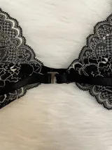 Conjunto de lencería de encaje negro con blanco, compuesto por un corpiño triangular con breteles regulables y cierre de gancho delantero, y una tanga regulable.