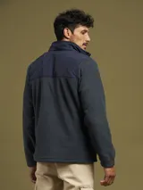 Campera de micropolar gris con detalles en negro en la parte superior y cuello. Tiene cierre frontal, bolsillos laterales con cierre y un bolsillo en el pecho con cierre.
