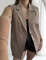 Chaleco largo color beige, de corte sastrero, con solapas, bolsillos delanteros y cierre con botones.