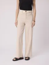 Pantalón de vestir color beige, de corte recto, con bolsillos laterales y traseros. Se ajusta a la cintura con cinturón de cuero marrón.