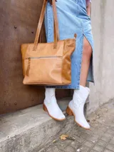 Bolso tipo tote de cuero color camel con paneles laterales texturizados. Tiene doble asa de hombro, cierre superior con cremallera y bolsillos internos.