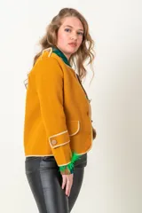 Chaqueta de tejido plano color mostaza, con vivos dorados y corte ajustado.