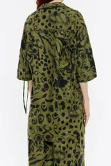 Camisa oversize de lino color verde con estampado animal en negro, cuello camisero con solapas, manga corta con cordones en sisa para ajustar y cierre frontal de botonadura.