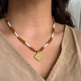 Collar de cuentas facetadas color ámbar, cuentas cilíndricas blancas y detalles dorados. Dije dorado con la imagen de San Benito.