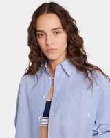 Camisa oversize celeste y blanca a rayas verticales, de popelina 100% algodón, con cuello clásico, bolsillo en el pecho bordado y puños abotonados.