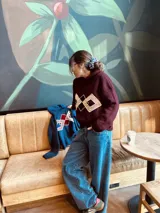 Sweater tejido color borgoña con cuello alto y diseño geométrico en el pecho en color crema.